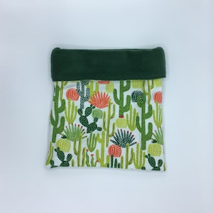May include: A square, fabric item with a white background and a pattern of green and orange cacti. The top edge is a solid dark green. The item is likely a storage bag or pillowcase.