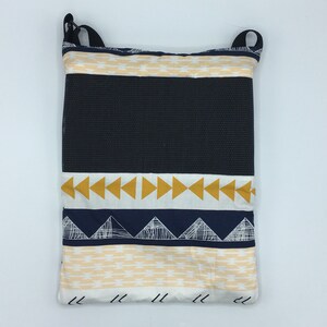 May include: A rectangular tote bag with a black mesh center panel and patterned fabric accents. The fabric features geometric designs in navy, mustard yellow, and cream. The bag has black straps for carrying.