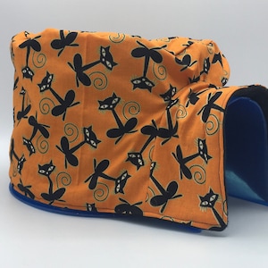 May include: A cat bed with a soft orange fabric exterior featuring a black cat pattern. The bed has a blue plastic base and a black fleece lining.