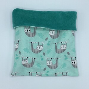 May include: A teal and white sloth-themed baby blanket. The blanket features a repeating pattern of gray sloths hanging from branches on a light teal background. The top edge is folded over, revealing a teal fleece lining.