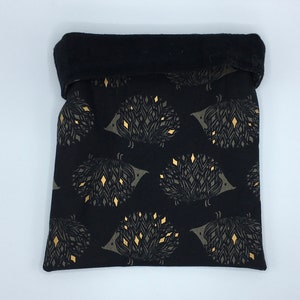 May include: Black fabric pouch with a repeating pattern of stylized hedgehogs in gray and gold. The top edge is folded over, revealing a black interior. The pouch is likely used for storage or carrying small items.