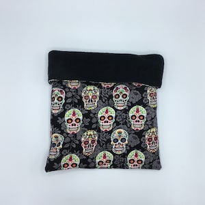May include: A black and gray fleece-lined pet bed with a sugar skull pattern. The skulls are colorful and have floral details.