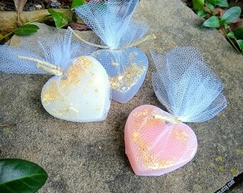 May include: Three heart-shaped soaps with gold flecks, wrapped in white tulle and tied with twine. The soaps are on a gray stone surface.