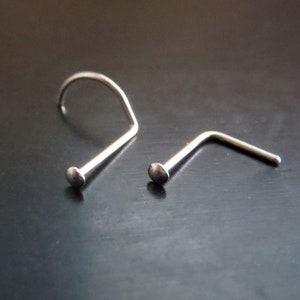 May include: Two silver nose rings, one with a curved L-shape and the other with a straight post and a small ball at the end.
