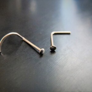 May include: Two silver nose rings, one is a straight L-shaped ring and the other is a curved ring.