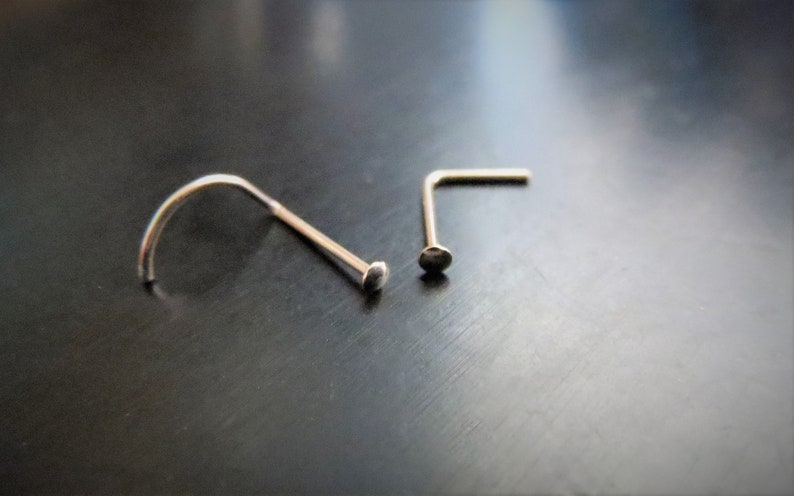 May include: Two silver nose rings, one is a straight L-shaped ring and the other is a curved ring.