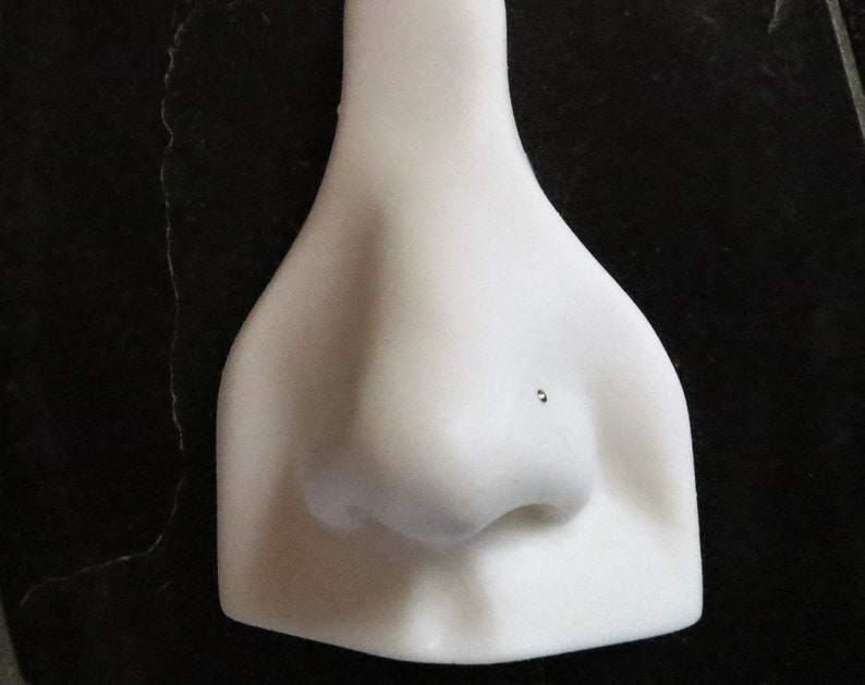 May include: White plastic nose ring display stand with a small hole for a nose ring.