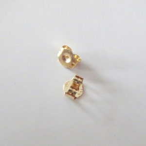 Peut inclure: Deux dos d'oreille en or. Les dos sont en m&eacute;tal et ont un petit trou au centre. Les dos sont con&ccedil;us pour &ecirc;tre utilis&eacute;s avec des boucles d'oreilles &agrave; tige.