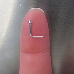 May include: A silver nose ring with a small ball at the end. The ring is bent at a 90-degree angle.