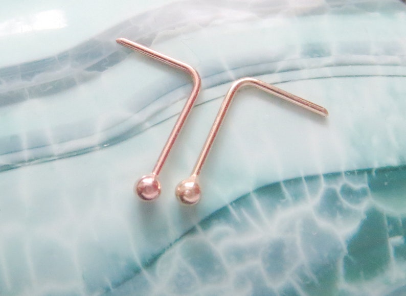May include: Two silver nose rings with a small ball at the end of each ring.