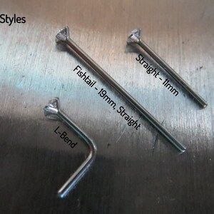 May include: Three nose ring post styles: a 19mm straight post, a 1mm straight post, and an L-bend post. The posts are made of metal and have a clear gemstone at the top.