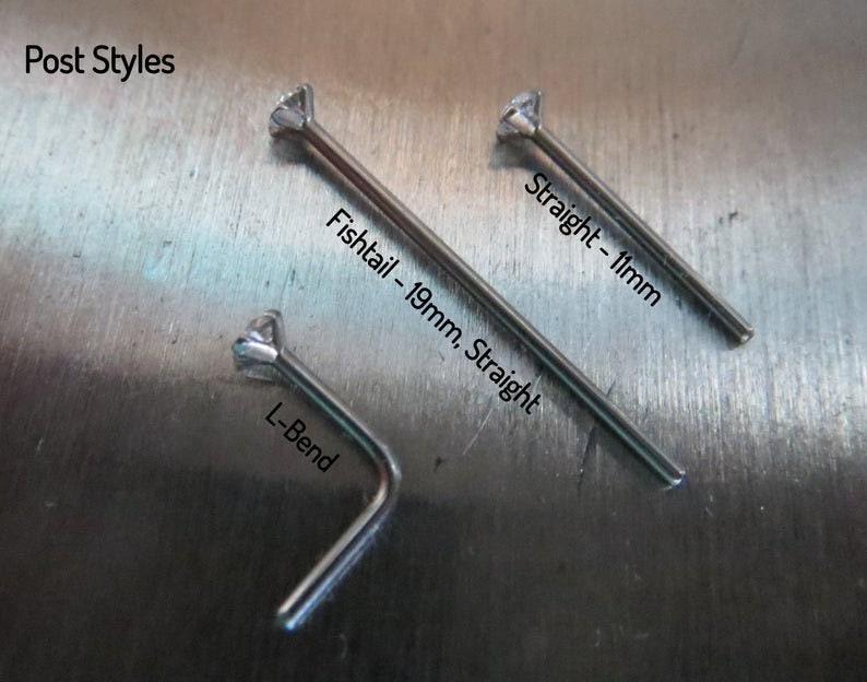 May include: Three nose ring post styles: a 19mm straight post, a 1mm straight post, and an L-bend post. The posts are made of metal and have a clear gemstone at the top.