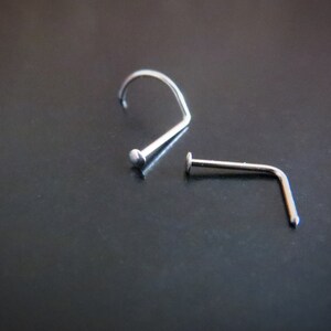 May include: Two silver nose rings, one with a curved shape and the other with a straight shape.