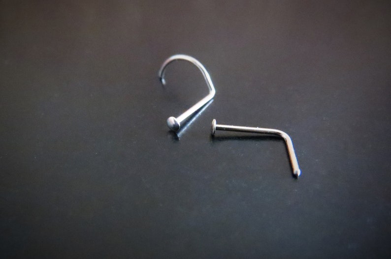 May include: Two silver nose rings, one with a curved shape and the other with a straight shape.