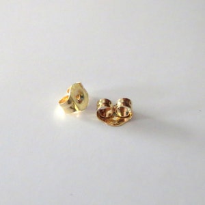 Peut inclure: Deux dos d'oreille en or. Les dos sont en m&eacute;tal et ont un petit trou au centre. Ils sont con&ccedil;us pour &ecirc;tre utilis&eacute;s avec des boucles d'oreilles &agrave; tige.
