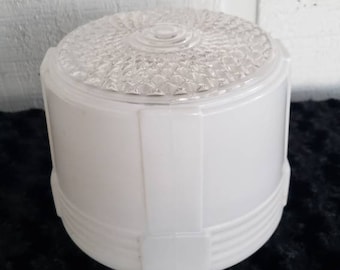 May include: A white, cylindrical light fixture with a clear, textured glass top. The fixture has a geometric design with horizontal and vertical lines. The base is a solid white color, and the top is a clear, patterned glass.