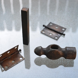 Peut inclure: Ensemble d'outils de menuiserie anciens, comprenant deux charnières métalliques, un petit marteau à panne ronde et une pièce rectangulaire en bois. Les outils ont un aspect rustique et vieilli de couleur marron.