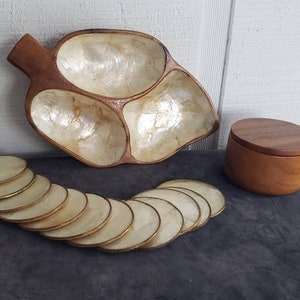Puede incluir: Una bandeja de madera con tres compartimentos nacarados, un recipiente de madera con tapa y un juego de posavasos redondos con borde dorado. El conjunto es de madera.