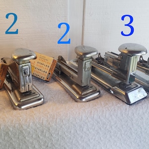 May include: Four vintage silver staplers with a box of staples. The staplers are numbered 1, 2, 2, 3, and 4.