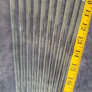 Op de afbeelding: Negen heldere glazen roerstaafjes met afgeronde uiteinden. De staafjes zijn ongeveer 15 cm lang en zijn in een waaier vorm gerangschikt. Een gele meetlint is zichtbaar op de achtergrond.