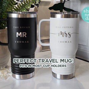 May include: Two travel mugs, one black and one white, with silver accents. The black mug reads "THE LUCKY MR THOMAS", and the white mug reads "THE FUTURE mrs THOMAS". Both mugs have handles and the text "PERFECT TRAVEL MUG! FITS IN MOST CUP HOLDERS".