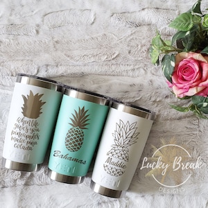 May include: Three stainless steel tumblers with a white and turquoise design. The tumblers feature a pineapple graphic and text that reads "When life gives you pineapples, make a pina colada", "Bahamas", and "Maddie".