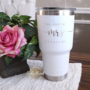 May include: White insulated tumbler with a silver rim and lid. The text "THE FUTURE mrs OTTAIANO" is printed on the front. A pink rose and green foliage are in the background. The tumbler has a silver base.