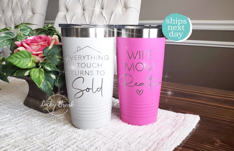 May include: Two stainless steel tumblers with a white and pink finish. The white tumbler has the text "Everything I touch turns to Sold" with a house icon. The pink tumbler has the text "Wife Mom Realtor" with a pink heart.