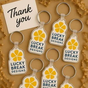 May include: Seven yellow and white keychains with a flower design and the text "Lucky Break Designs".