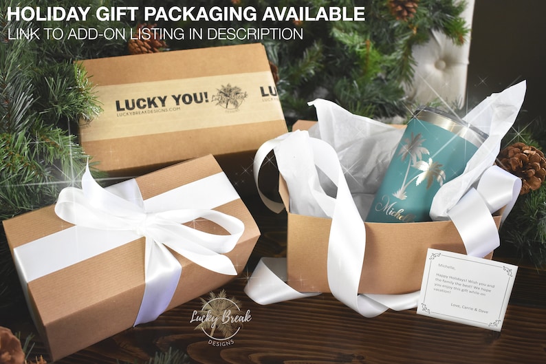 May include: Gift set with a teal tumbler featuring palm tree designs and a personalized name, nestled in a kraft paper box with white ribbon. The box is inside a larger gift box with a white ribbon. The image includes a holiday card.