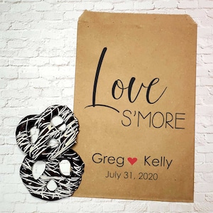 May include: Brown paper bag with the text "Love S'more" and the names "Greg Kelly" with a red heart symbol between them. The date "July 31, 2020" is printed below the names. Two chocolate-covered pretzels are in the foreground.