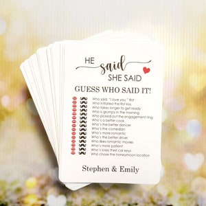 May include: A white card game with red lips and mustaches printed on it. The text on the card reads "HE said SHE SAID GUESS WHO SAID IT!" and includes a list of questions about a couple's relationship. The card is personalized with the names "Stephen & Emily".