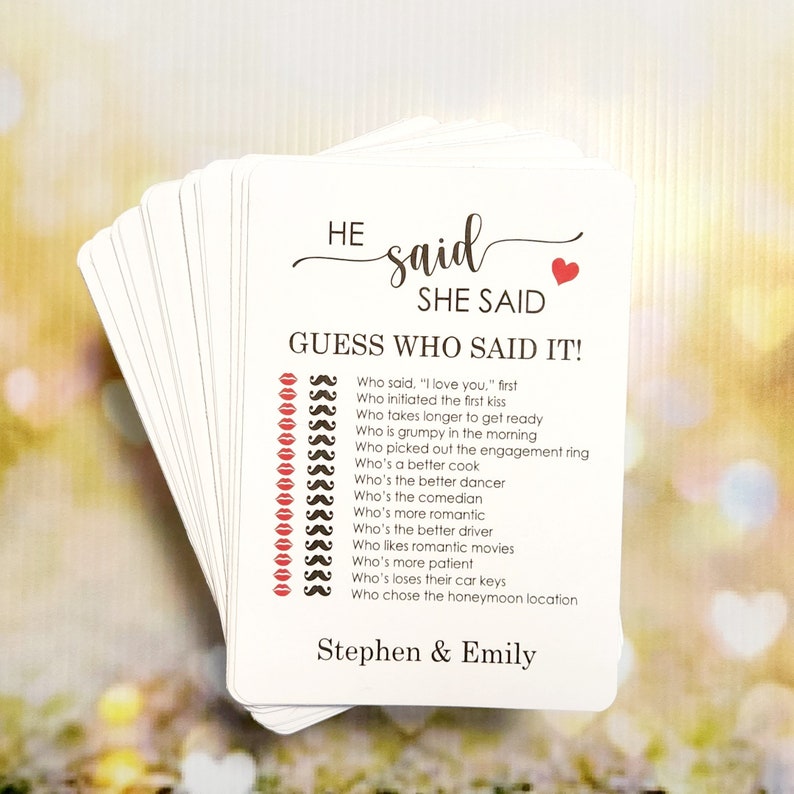 May include: A white card game with red lips and mustaches printed on it. The text on the card reads "HE said SHE SAID GUESS WHO SAID IT!" and includes a list of questions about a couple's relationship. The card is personalized with the names "Stephen & Emily".