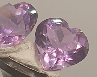 Könnte beinhalten: Zwei herzförmige Amethyst-Edelsteine mit einem hellvioletten Farbton und einem facettierten Schliff.
