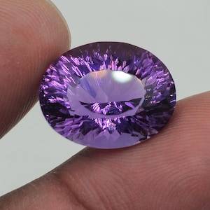 Peut inclure: Une grande gemme d'améthyste de forme ovale, de couleur violet foncé. La gemme est taillée à facettes et présente un haut degré de brillance.