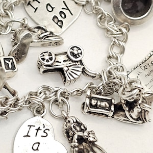 May include: A silver charm bracelet with various charms, including a heart charm that says "It's a Boy", a heart charm that says "It's a Girl", a baby carriage charm, and a baby angel charm.