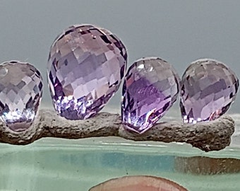 May include: Four faceted amethyst gemstones in a teardrop shape, arranged on a branch-like piece of wood.