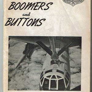 May include: A black and white photo of a bomber plane in flight. The plane is flying over clouds. The text "Bombers Boomers and Buttons" is printed on the cover of the book. The Strategic Air Command logo is in the top right corner.