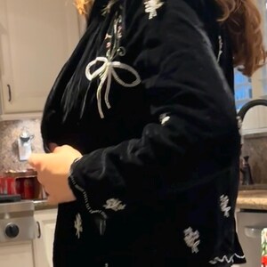 May include: Black velvet jacket with white floral and bow embroidery. The jacket features a scalloped hem and detailed embellishments. A stylish outerwear piece.
