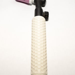 May include: A TIG welding torch handle featuring a white cylindrical grip with a textured honeycomb pattern and the embossed text NGP at the base. The torch includes a black neck assembly and a pink ceramic gas nozzle with the number 10 printed on it.
