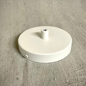 May include: White ceiling mount for a pendant light fixture. The mount has a round base and a threaded center hole for attaching the light fixture.
