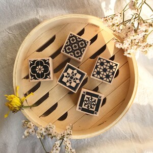 May include: Five wooden stamps with black and white geometric designs. The stamps are arranged in a circle on a wooden surface.