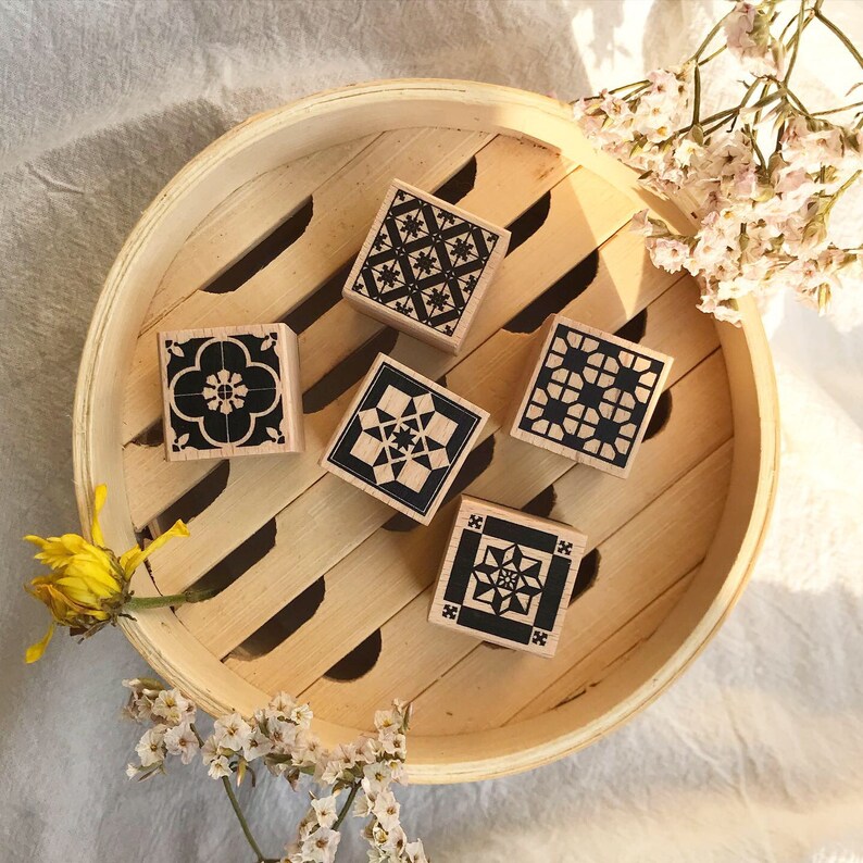 May include: Five wooden stamps with black and white geometric designs. The stamps are arranged in a circle on a wooden surface.