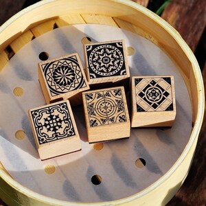 May include: Five wooden stamps with black and white geometric designs in a light brown bamboo steamer.