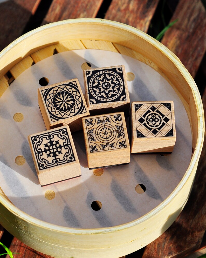 May include: Five wooden stamps with black and white geometric designs in a light brown bamboo steamer.