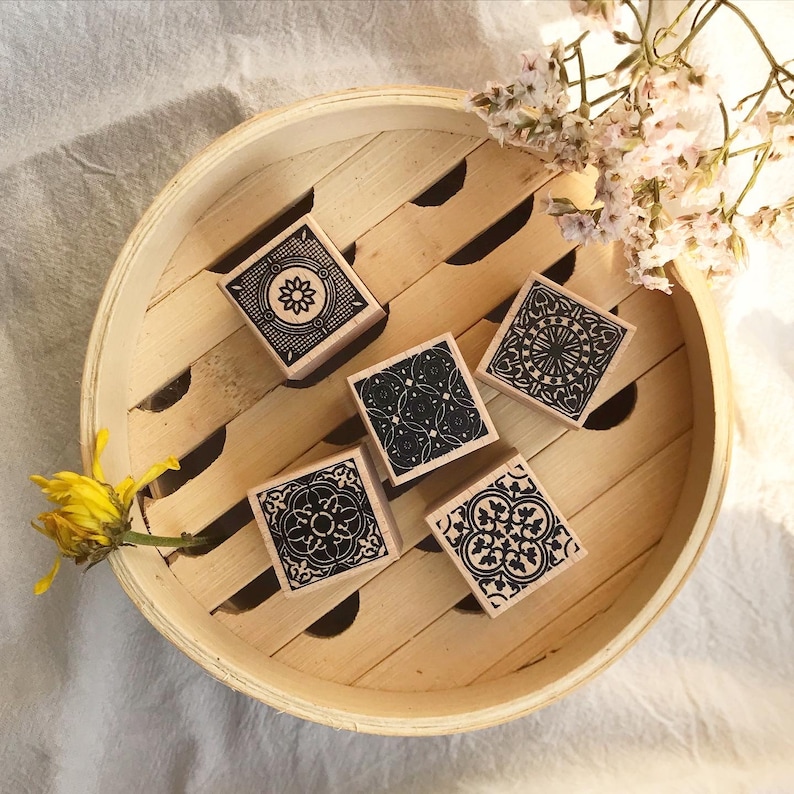 May include: Five wooden stamps with black and white geometric designs. The stamps are arranged in a circle on a wooden surface.