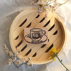 May include: A wooden stamp with a black and white illustration of a teacup and saucer with floral designs.