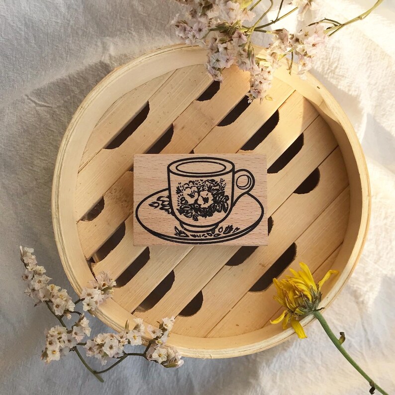 May include: A wooden stamp with a black and white illustration of a teacup and saucer with floral designs.