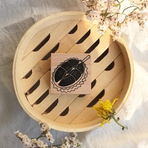May include: A wooden stamp with a black and white illustration of a durian fruit. The stamp is sitting on a wooden surface.