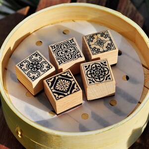 May include: Five wooden stamps with black and white geometric designs, arranged in a circle on a white surface inside a round wooden container.